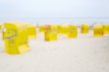 Eine Fotografie ohne Titel, sie zeigt verschwommene gelbe Strandkörbe am Strand